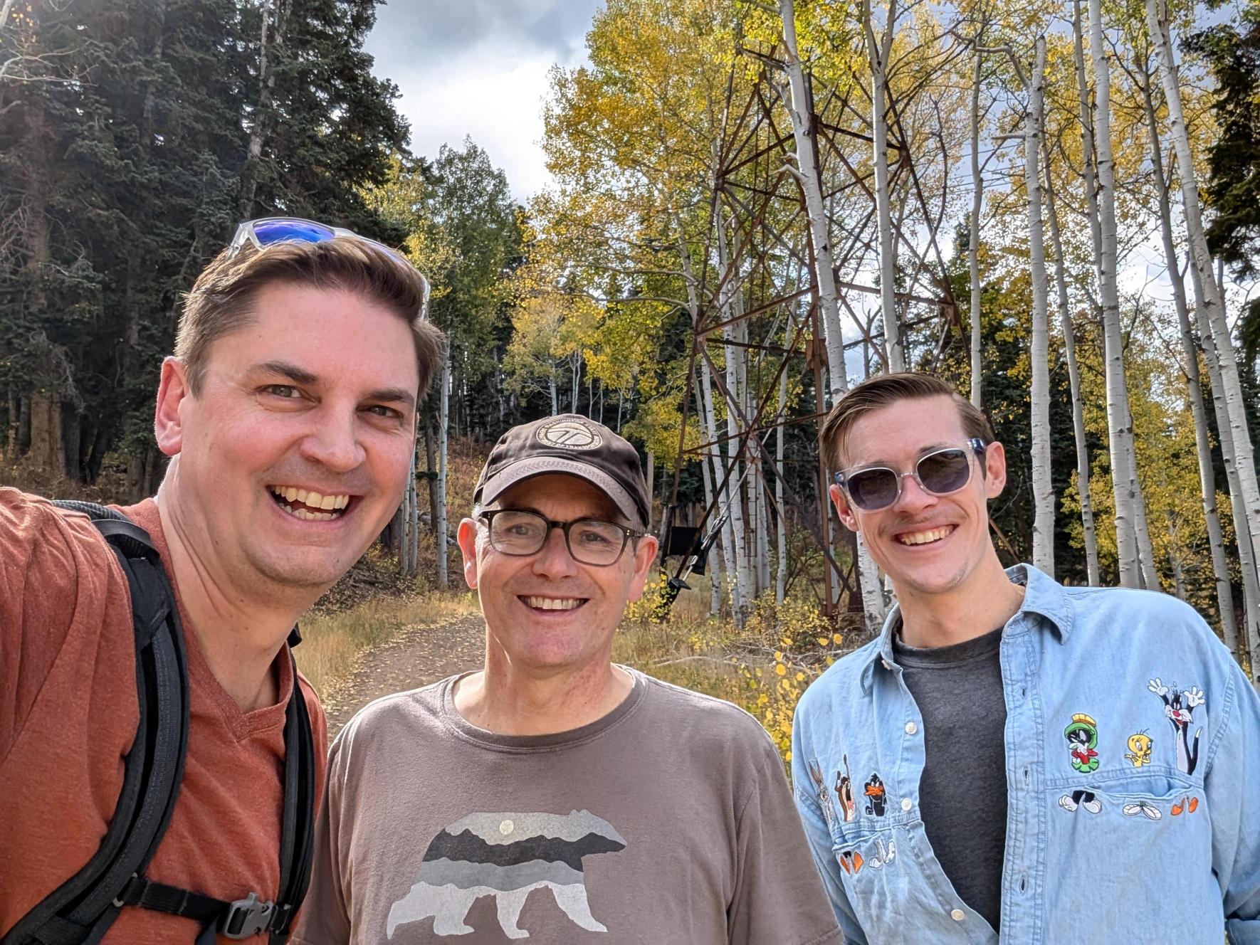Three people smiling outdoors in autumn forest.
