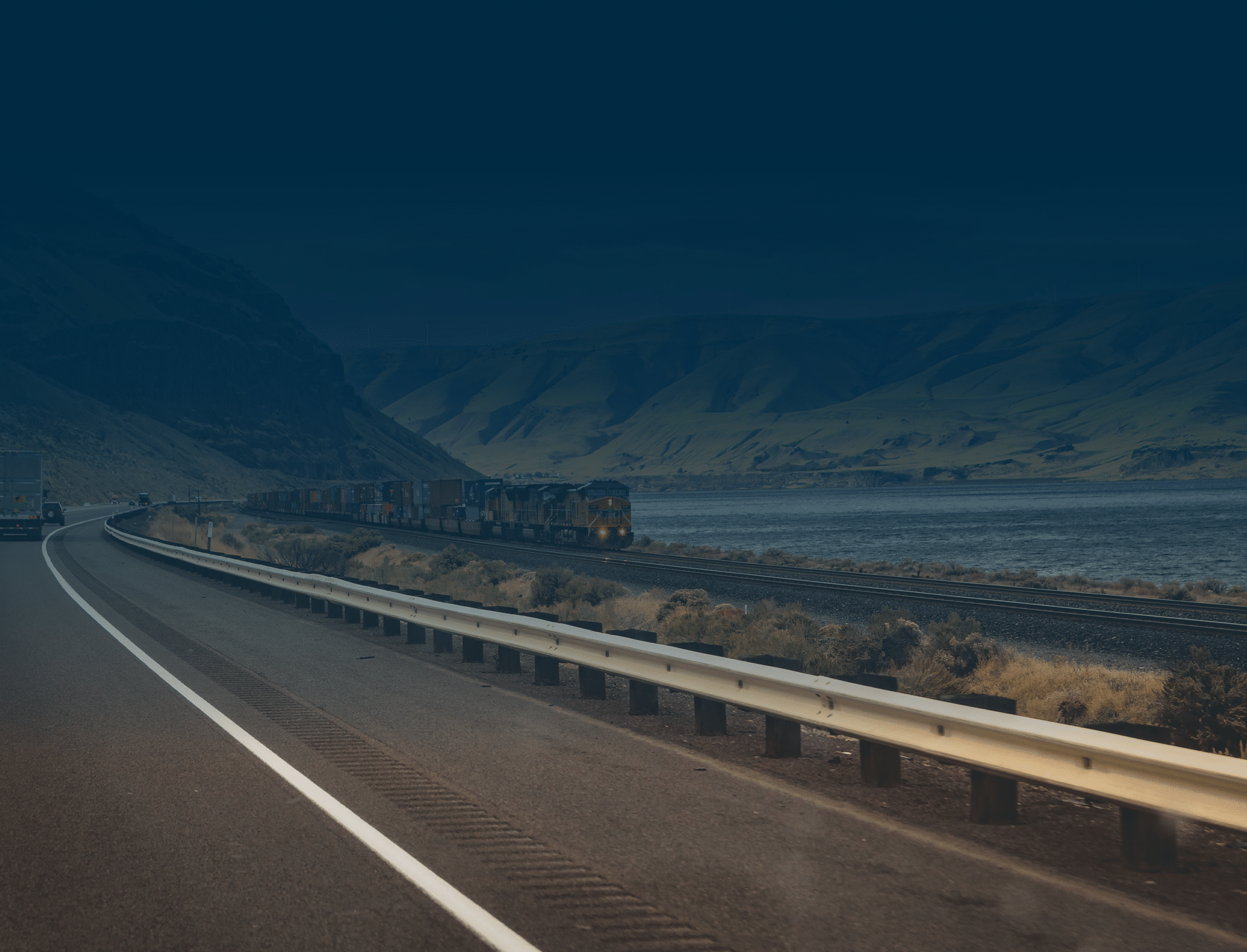 Highway and train along river under mountains.